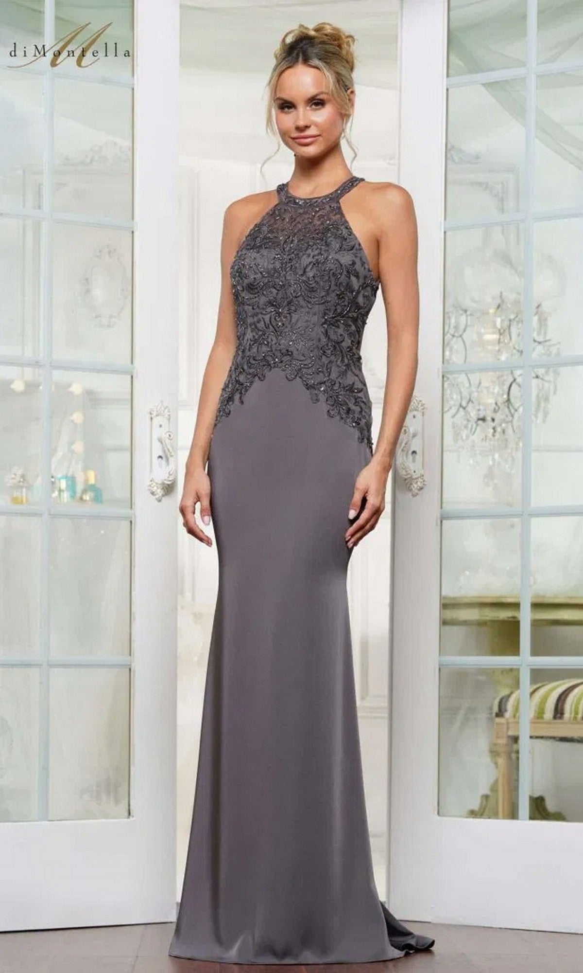A woman stands indoors wearing the Long Formal Dress: Rina Di Montella RD2755—a sleeveless, floor-length gray gown with lace details and a sophisticated, fitted silhouette.